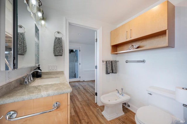 bathroom featuring toilet, a bidet, vanity, wood finished floors, and baseboards