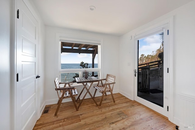 dining area featuring a water view, light wood-style floors, plenty of natural light, and visible vents