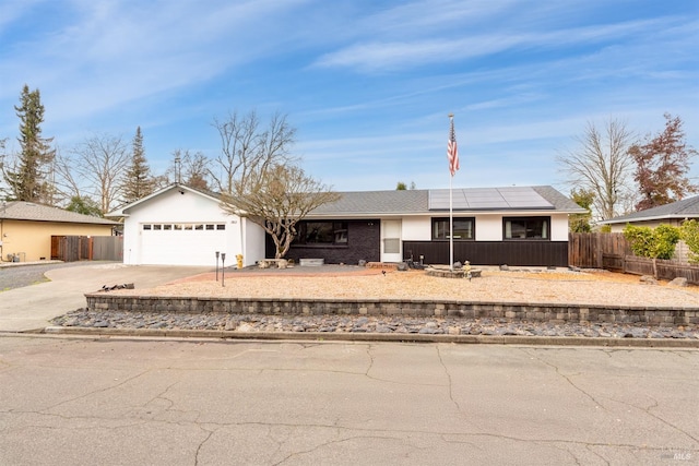 ranch-style house featuring a garage, concrete driveway, fence, and roof mounted solar panels