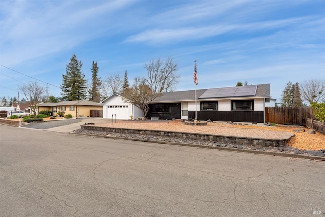 ranch-style house featuring driveway, an attached garage, roof mounted solar panels, and fence