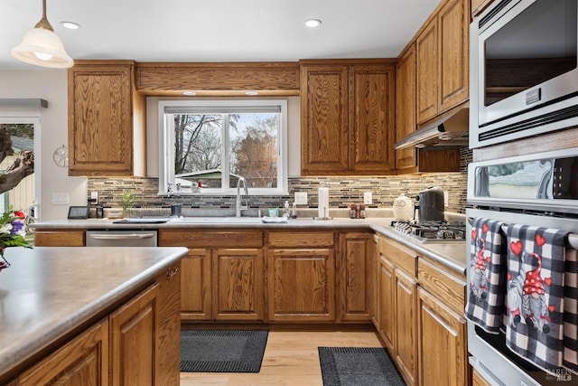 kitchen featuring a sink, stainless steel appliances, under cabinet range hood, and brown cabinets
