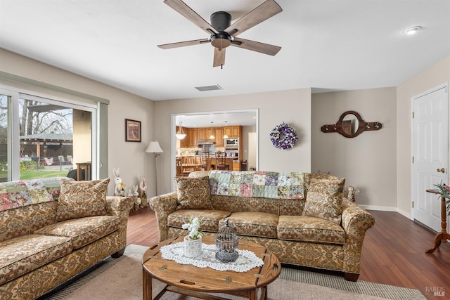 living room with a ceiling fan, wood finished floors, baseboards, and visible vents