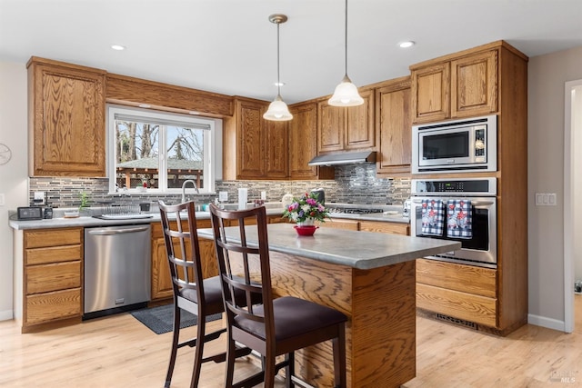 kitchen with a center island, under cabinet range hood, backsplash, light wood-style flooring, and appliances with stainless steel finishes