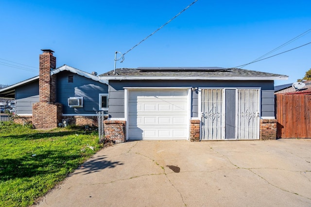 garage featuring driveway, an AC wall unit, fence, and roof mounted solar panels