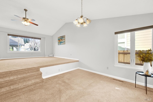 carpeted empty room featuring lofted ceiling, ceiling fan with notable chandelier, and a wealth of natural light