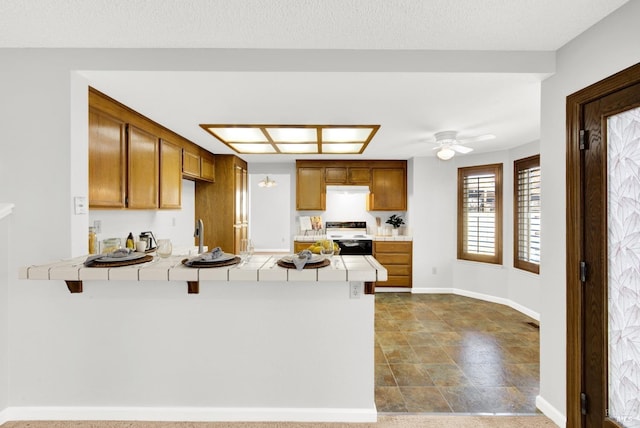 kitchen featuring a breakfast bar area, tile countertops, kitchen peninsula, range with electric cooktop, and ceiling fan