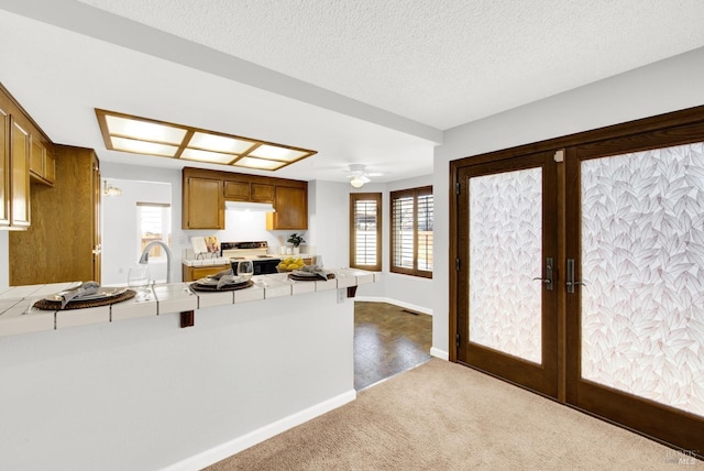 kitchen with carpet, tile counters, electric range, kitchen peninsula, and french doors