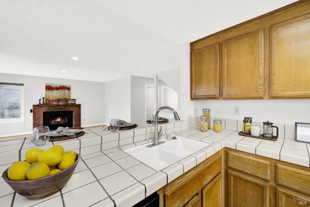 kitchen with a brick fireplace, sink, tile counters, and a textured ceiling