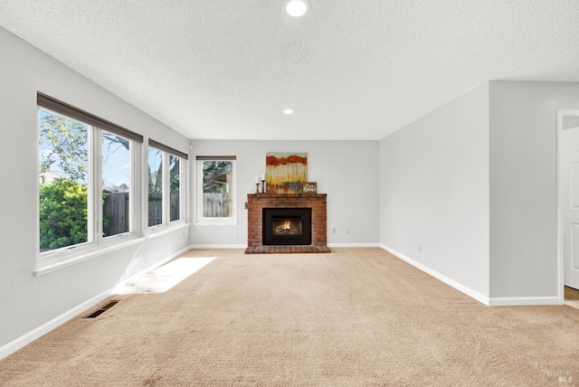 unfurnished living room featuring light colored carpet, a brick fireplace, and a textured ceiling