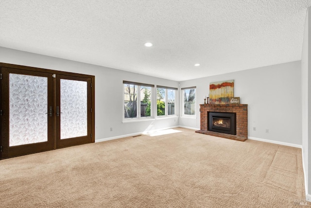 unfurnished living room with french doors, a brick fireplace, light carpet, and a textured ceiling