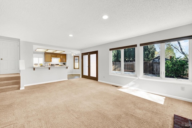 unfurnished living room with light carpet, french doors, and a textured ceiling