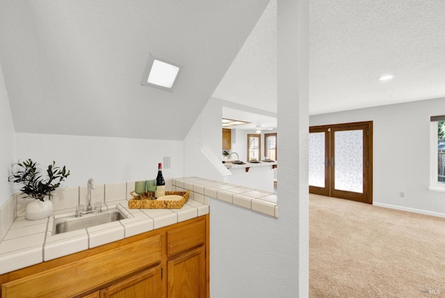 kitchen featuring lofted ceiling, sink, tile counters, a textured ceiling, and light carpet