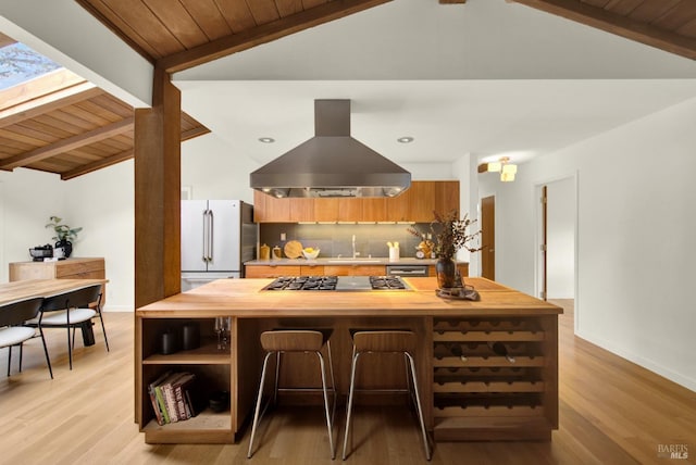 kitchen featuring vaulted ceiling with beams, freestanding refrigerator, butcher block countertops, island range hood, and stainless steel gas stovetop