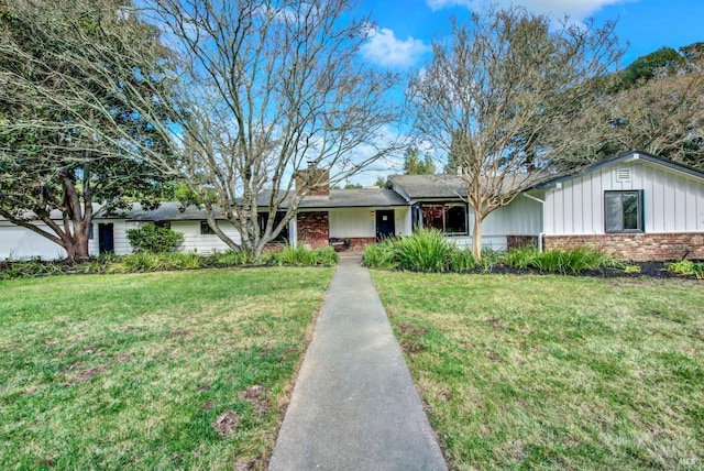 ranch-style house featuring a chimney, a front lawn, brick siding, and board and batten siding