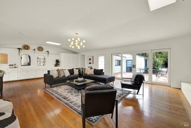 living area with wood finished floors, lofted ceiling with skylight, and a chandelier