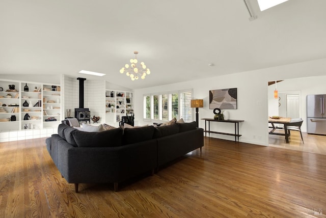 living area with a chandelier, vaulted ceiling, a wood stove, and wood finished floors