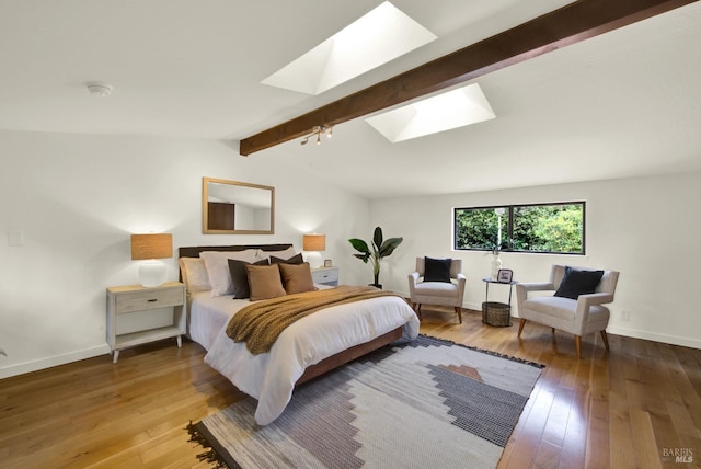 bedroom featuring wood-type flooring, vaulted ceiling with skylight, and baseboards