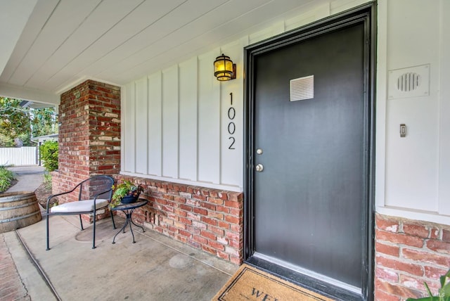 doorway to property featuring brick siding, a porch, and board and batten siding