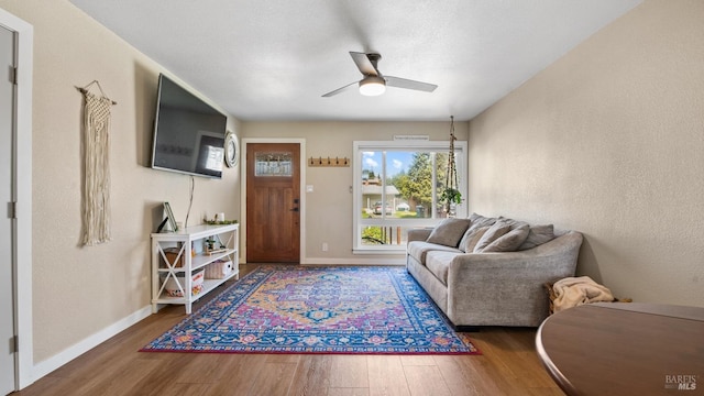 living area featuring baseboards, a ceiling fan, wood finished floors, and a textured wall