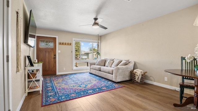 living room with a textured ceiling, wood finished floors, a ceiling fan, and baseboards