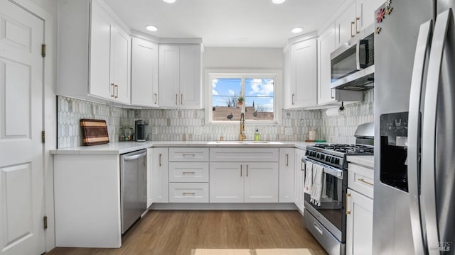 kitchen with stainless steel appliances, light countertops, light wood-type flooring, white cabinetry, and a sink