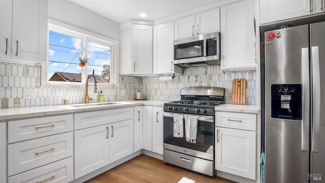 kitchen with wood finished floors, a sink, white cabinets, appliances with stainless steel finishes, and backsplash