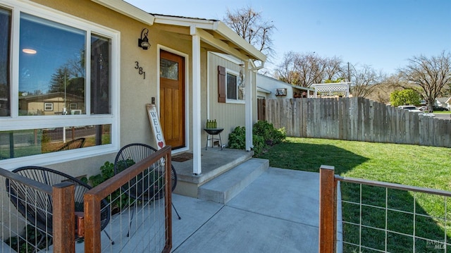 property entrance featuring stucco siding, fence, and a lawn