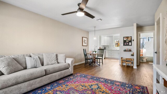 living area with baseboards, light wood finished floors, visible vents, and a ceiling fan