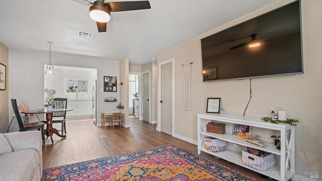 living room featuring baseboards, ceiling fan, visible vents, and wood finished floors