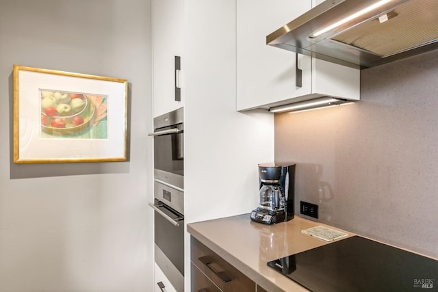 kitchen featuring black electric cooktop, stainless steel double oven, extractor fan, and white cabinets