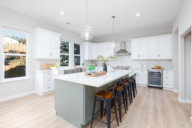 kitchen featuring decorative light fixtures, white cabinets, wine cooler, a center island, and wall chimney range hood