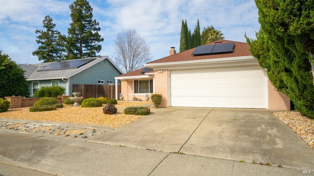 single story home featuring a garage, solar panels, brick siding, fence, and driveway