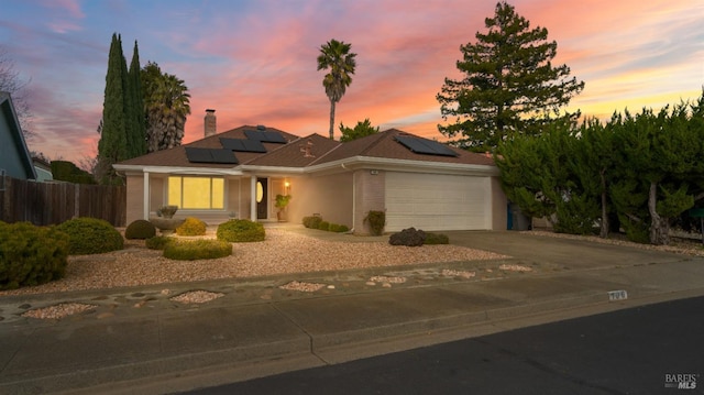 view of front of home featuring a chimney, solar panels, an attached garage, fence, and driveway