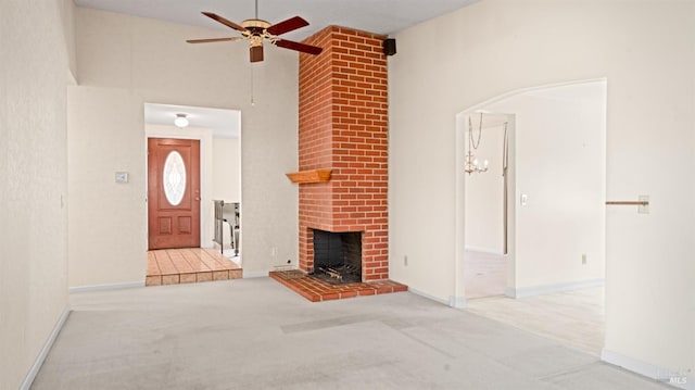 unfurnished living room with arched walkways, a fireplace, a towering ceiling, light carpet, and ceiling fan