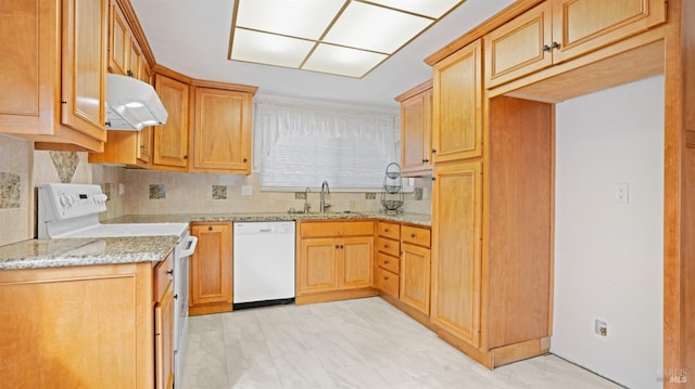 kitchen with light stone counters, under cabinet range hood, white appliances, a sink, and tasteful backsplash