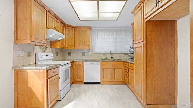 kitchen featuring white appliances, tasteful backsplash, light stone counters, under cabinet range hood, and a sink