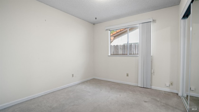 empty room featuring light carpet, a textured ceiling, and baseboards