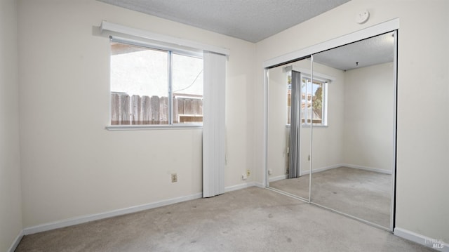 unfurnished bedroom featuring a textured ceiling, a closet, baseboards, and light colored carpet