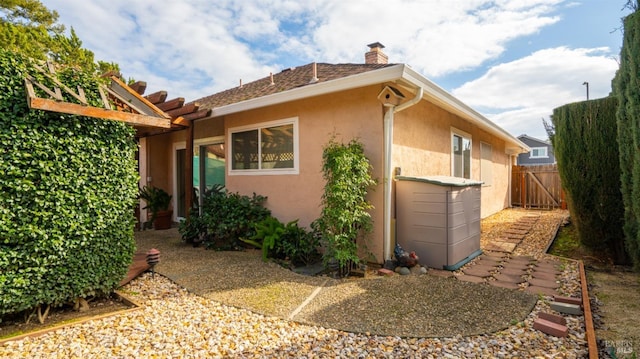 view of property exterior with a chimney, fence, and stucco siding