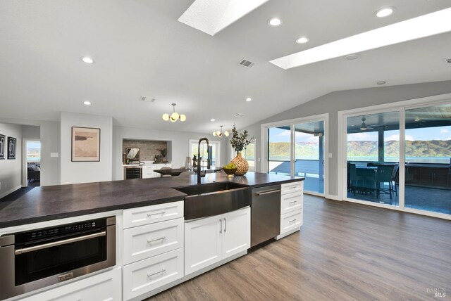 kitchen featuring sink, hardwood / wood-style flooring, white cabinetry, stainless steel appliances, and vaulted ceiling with skylight