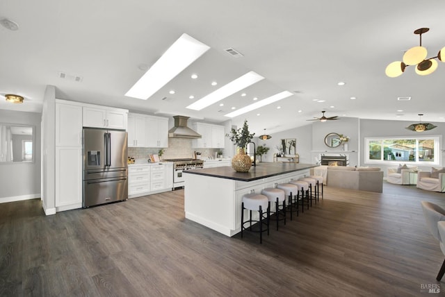 kitchen with a breakfast bar, appliances with stainless steel finishes, white cabinetry, custom range hood, and decorative light fixtures