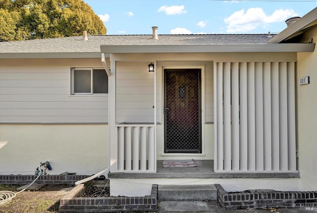 view of exterior entry featuring roof with shingles