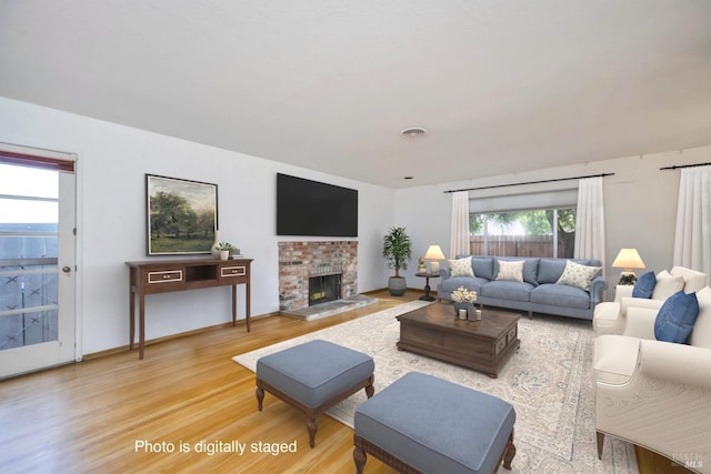 living room featuring visible vents, a brick fireplace, baseboards, and light wood-style floors