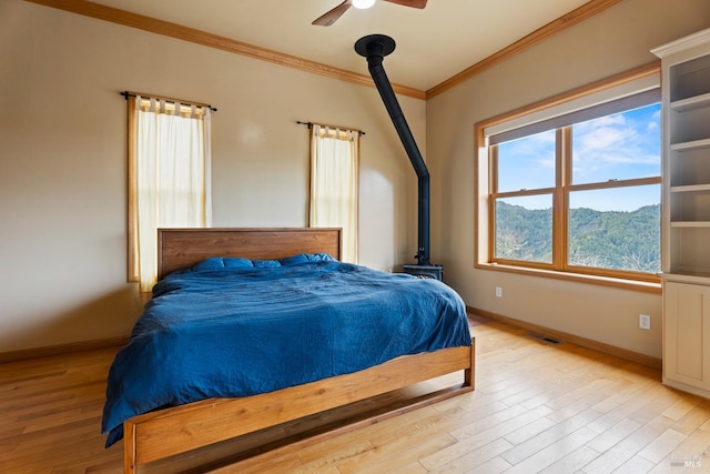 bedroom with a mountain view, ceiling fan, light hardwood / wood-style floors, crown molding, and a wood stove