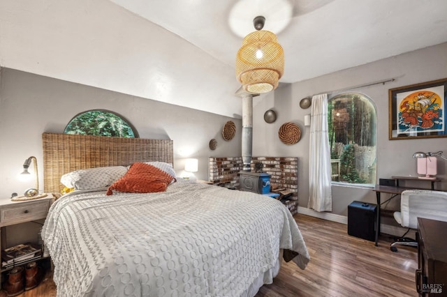 bedroom with lofted ceiling, hardwood / wood-style floors, multiple windows, and a wood stove