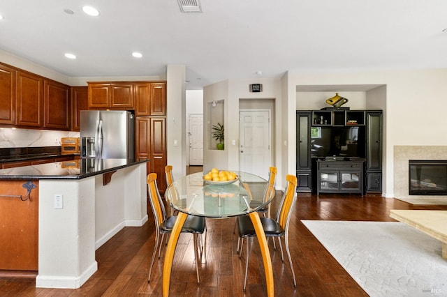 kitchen with recessed lighting, a premium fireplace, stainless steel refrigerator with ice dispenser, dark wood-style floors, and brown cabinetry