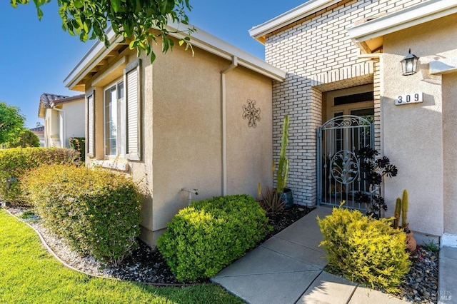 view of exterior entry featuring brick siding, a gate, and stucco siding