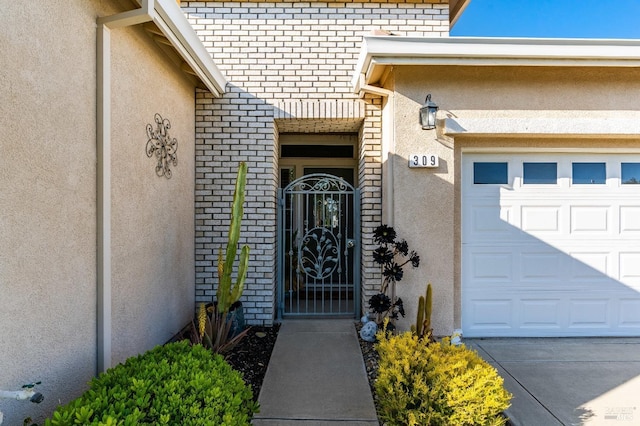 doorway to property featuring brick siding, a garage, stucco siding, and a gate