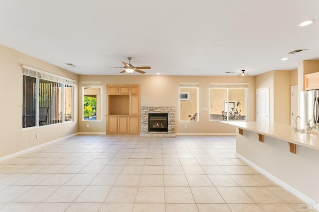 unfurnished living room featuring visible vents, baseboards, ceiling fan, and a fireplace