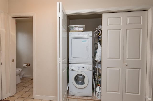 laundry area with light tile patterned floors, stacked washer and dryer, baseboards, and laundry area